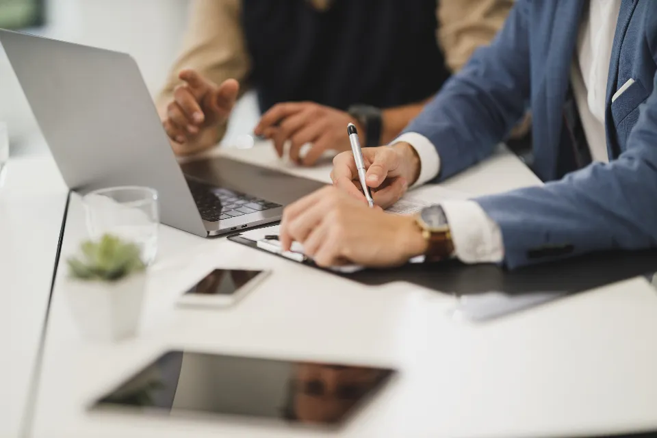 Un professionnel annote un dossier devant un ordinateur portable