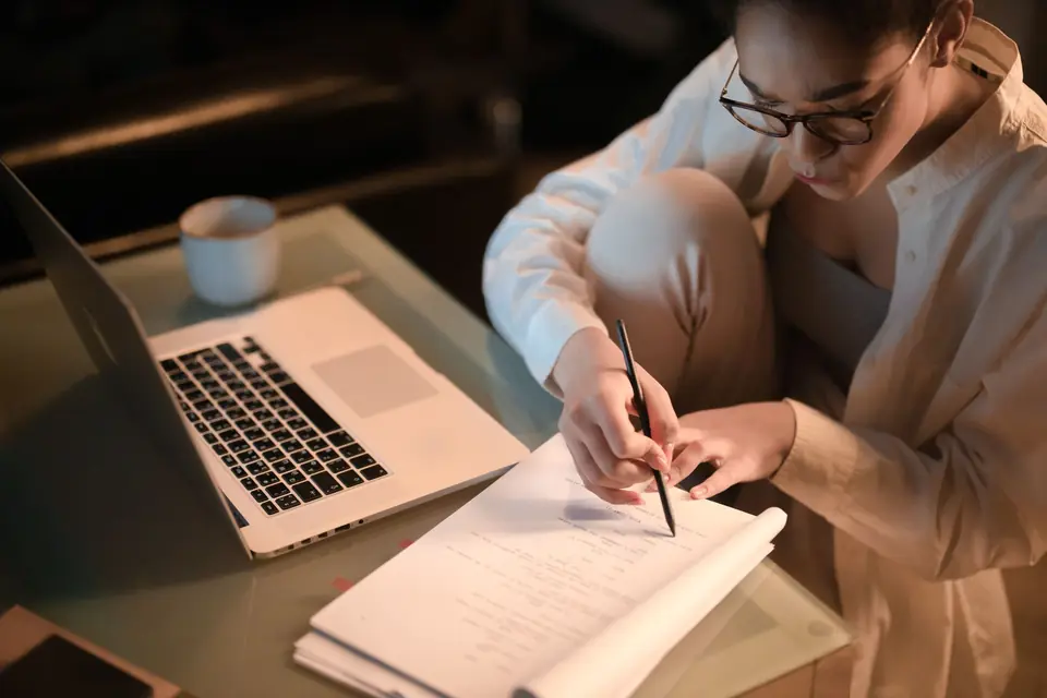 Une professionnelle prend des notes le soir devant son ordinateur