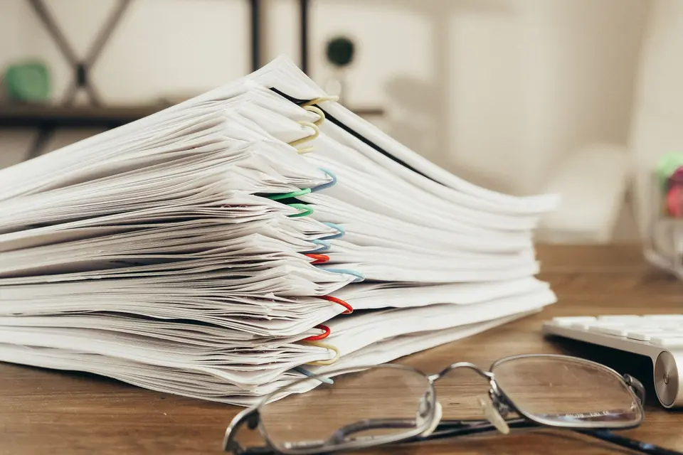 Pile de dossiers papier et lunettes posées sur un bureau